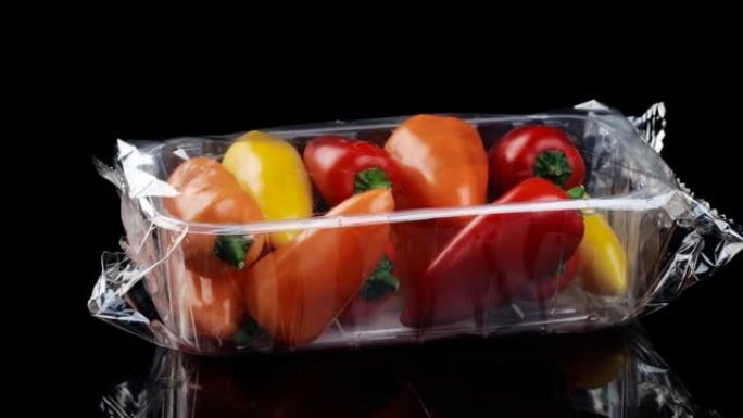 透明包装中的新鲜多汁甜椒在黑色背景上旋转