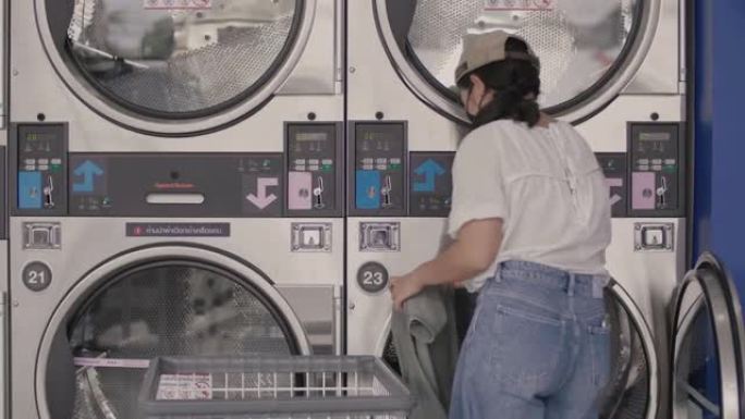 戴着口罩的年轻女子正在自动洗衣店洗衣服。