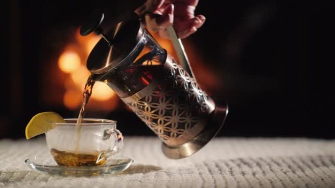 将茶倒入壁炉背景上的杯子中。在舒适的环境中喝茶