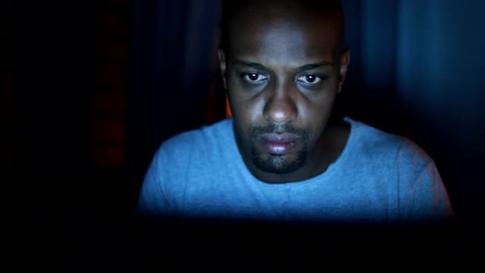 黑人男子晚上脸盯着笔记本电脑屏幕