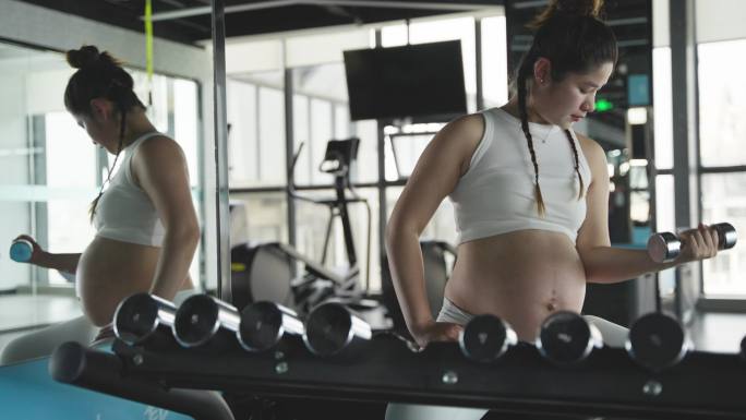 怀孕的妇女在健身房锻炼身体举哑铃撸铁