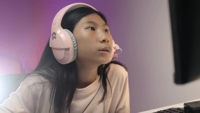 快乐的亚洲女孩戴着耳机，晚上在家铺设网络游戏，带发光二极管背景，生活理念。