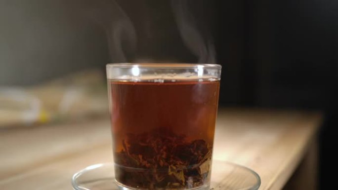 一杯新鲜冲泡的红茶放在木桌上，逸出蒸汽，温暖柔和的光线，深色的背景。在透明玻璃杯中新鲜冲泡的红茶，逸