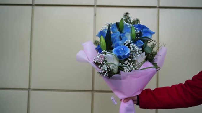 女人的手特写着五颜六色的花束。无法辨认的女性拿着包装纸上的蓝玫瑰和白百合的花朵组成