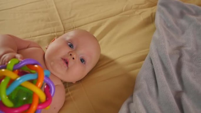 微笑的婴儿躺在床上，用手握住玩具，然后轻咬玩具。儿童的感觉发育。特写镜头。