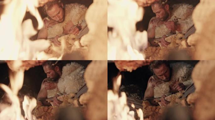 穿着原始羊皮的男人晚上坐在燃烧的篝火旁，用自己的肩膀伤口上的鲜血在石头上写字