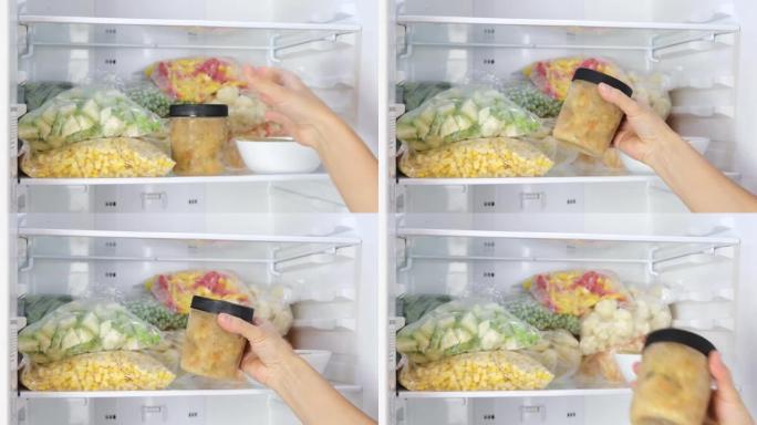 女性的手在冰箱里取出装有冷冻汤的容器。冷冻水果、蔬菜、肉放在冰箱里。