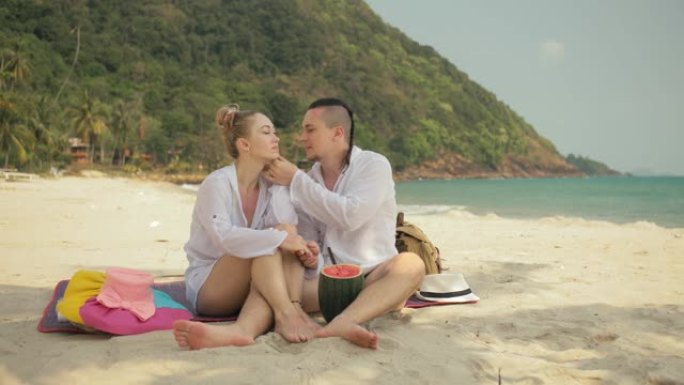 欢快的爱情夫妇在热带沙滩上拿着和吃西瓜片。浪漫的恋人两个人度过夏季周末。