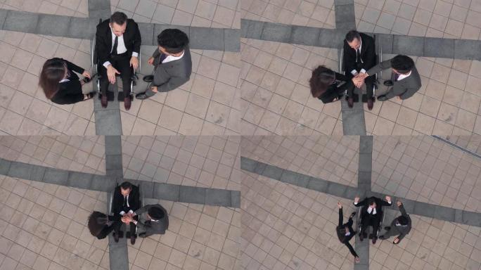 空中。三个穿着正式服装的同事在上班前开会，一个坐在轮椅上，到办公室里。顶视图。