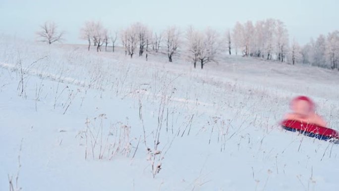 小女孩骑在户外小山上的充气雪橇上