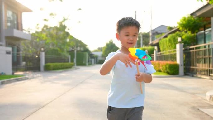 亚洲孩子在住宅区用彩色风车奔跑。纯真和自由的概念