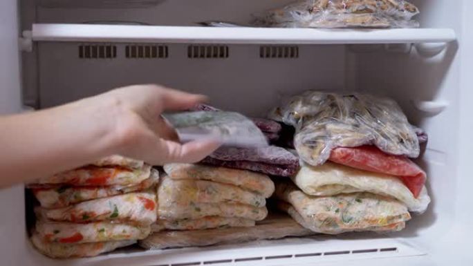 女性的手在冰箱中放置冷冻的蔬菜团块。冷冻蔬菜