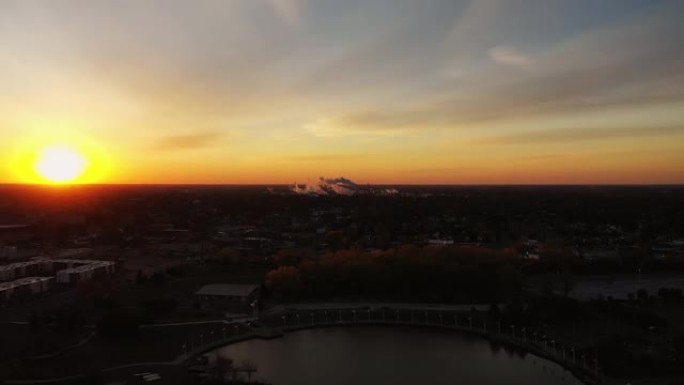 当明亮的橙色太阳升起在地平线上照亮天空，烟雾从地平线上喷出时，空中降落到俄亥俄州托莱多河上的海滨公园