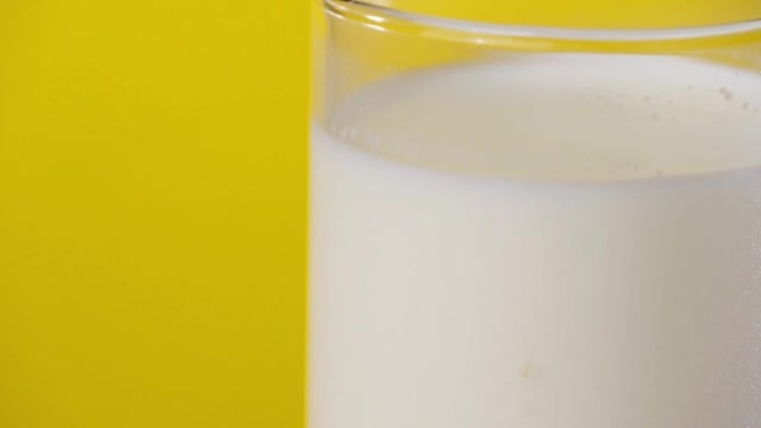 用手将牛奶倒入黄色背景的玻璃中。