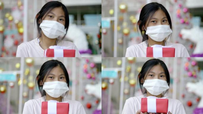 快乐的亚洲女孩戴着面具拿着红色礼品盒与圣诞节背景，节日概念。