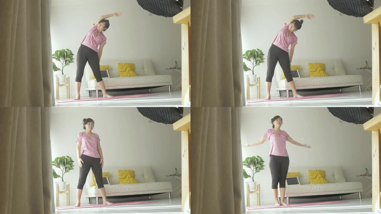 亚洲女性通过数字平板电脑在粉红色瑜伽垫上学习瑜伽，早晨在阳光照射下靠窗，在家中健康的生活方式理念。