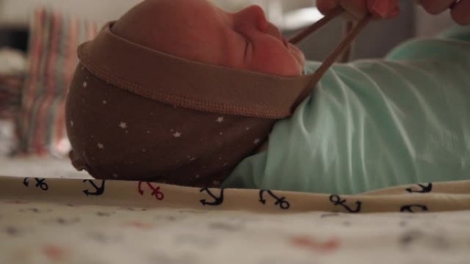 母亲襁褓着她刚出生的婴儿。把婴儿用尿布包起来。新生儿躺在床上。妈妈给孩子戴上帽子
