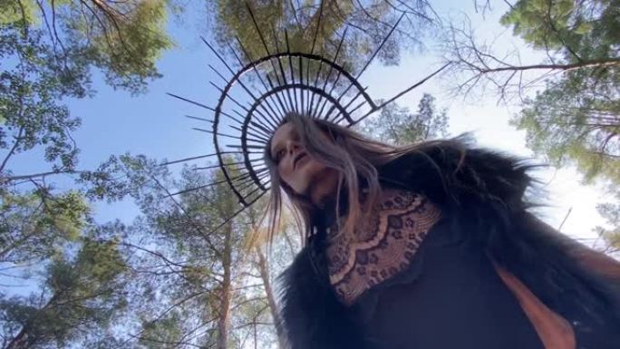 女巫形象的女人站在森林中树木和天空的背景下。