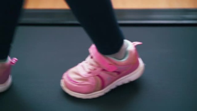 顽皮的女孩粉色运动鞋在家里的现代跑步机上跳跃