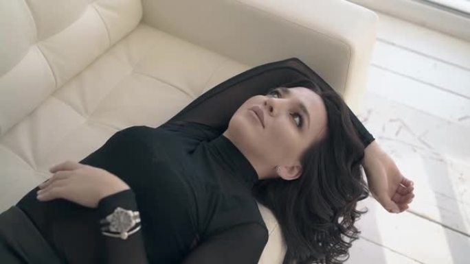 穿着黑色衬衫的女人喜欢在白色真皮沙发上休息