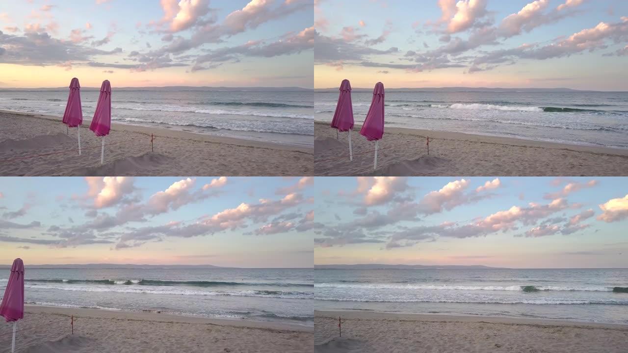 日落时分，沙滩上有两把红色的防晒伞，海浪。