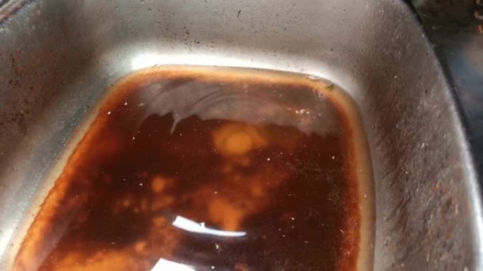 水龙头断了滴水。洗手盆水槽排水堵塞。食物残渣和咖啡弄脏了水槽。特写视图。