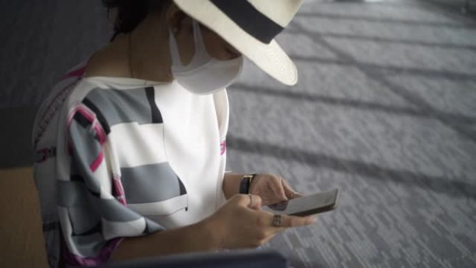 一名戴着防护口罩的亚洲年轻女性游客在国内机场等待航班时正在使用智能手机