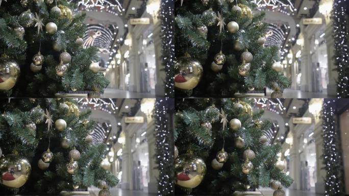 在商店橱窗的背景下，一棵装饰着金球的圣诞树矗立在购物中心的大厅里