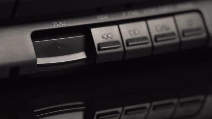 旧黑色录音带播放器上的播放按钮。这个人用手指按下播放按钮。特写按钮。上一代的旧技术。模拟设备