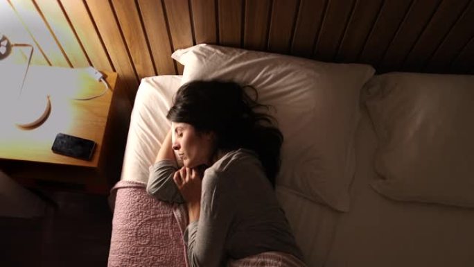躺在床上准备睡觉的女人。30岁的女人关掉床头柜床头灯