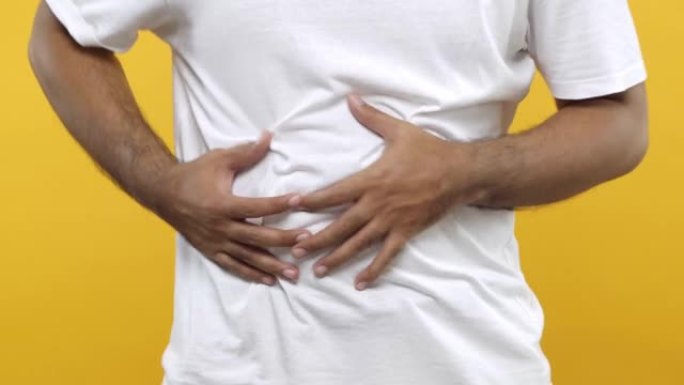 特写。男子用双手抱住他的胃，有胃炎发作或疼痛的痉挛，压在肚子上，痛苦的表情孤立在黄色的背景。