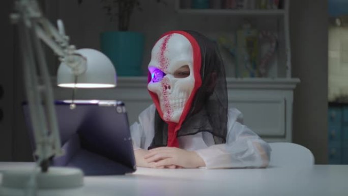 穿着万圣节骷髅服装的孩子，眼睛闪烁，通过平板电脑上的视频通话。检疫万圣节庆祝活动。在网上吓唬朋友的孩
