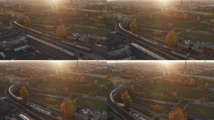 从空中角度看，地铁列车以黄色和橙色的秋天颜色和日落金色的光线穿过德国柏林的公园