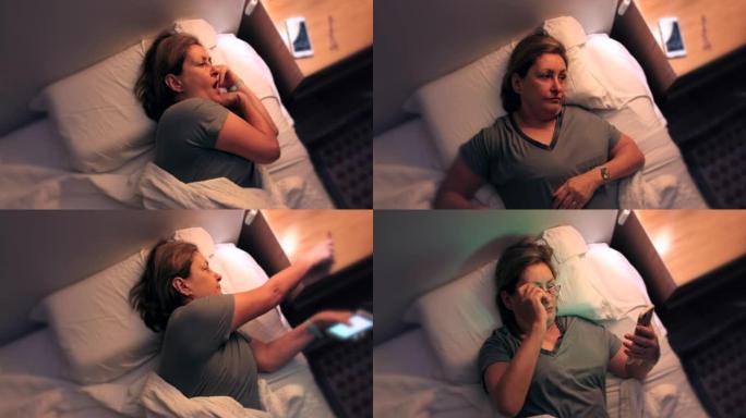 疲倦的女人半夜醒来无法入睡，打开床头柜的床灯并拿起电话