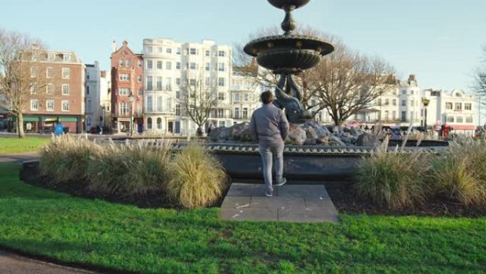 一个年轻人在绿色的老Steine花园里，有一个喷泉，在英国布赖顿，4k。