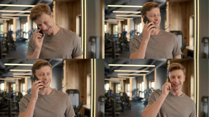 快乐的健身男子在体育俱乐部使用电话。健美运动员站在健身房。