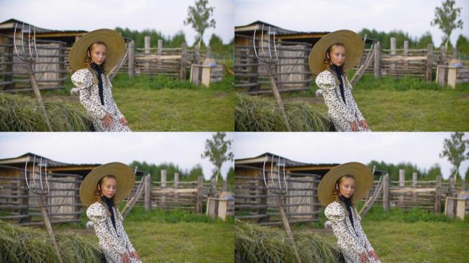 乡村的乡村女孩穿着复古连衣裙和帽子，以干草堆和干草叉为背景。乡村风景中的海瑞克帽子上的浪漫女孩肖像。