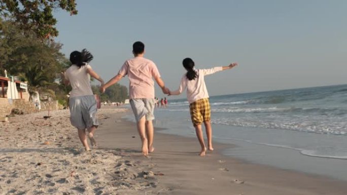 快乐的亚洲妈妈和孩子们早上带着阳光一起在海滩上奔跑，在泰国华欣度假。