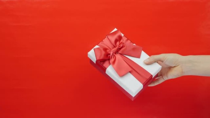 Hand显示白色盒子，红色背景上带有红丝带蝴蝶结。女性手里拿着情人节礼物。圣情人节、国际妇女节