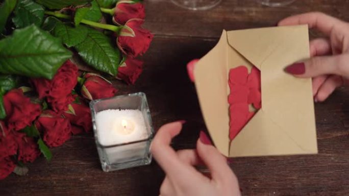 女人的手用心打开一封信。桌子上有玫瑰和蜡烛。情人节概念。