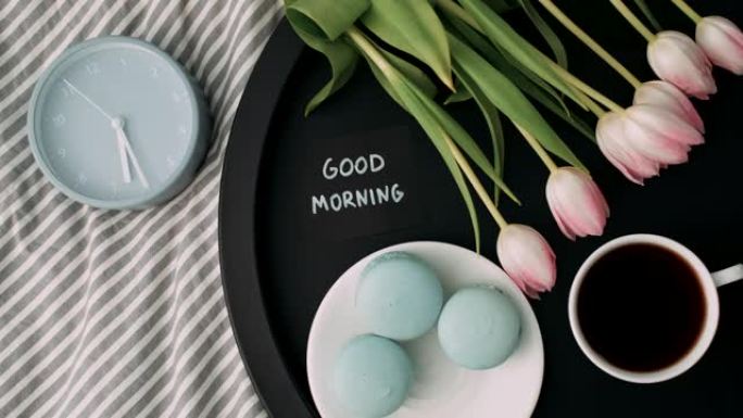 托盘上有法式马卡龙和新鲜郁金香的笔记 “早上好” 的俯视图，上午6:30点一杯咖啡和闹钟