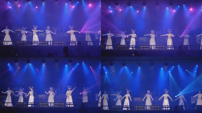 一组亚洲舞者，穿着白色和闪亮的连衣裙，在舞台上展示不同颜色的迪斯科灯光