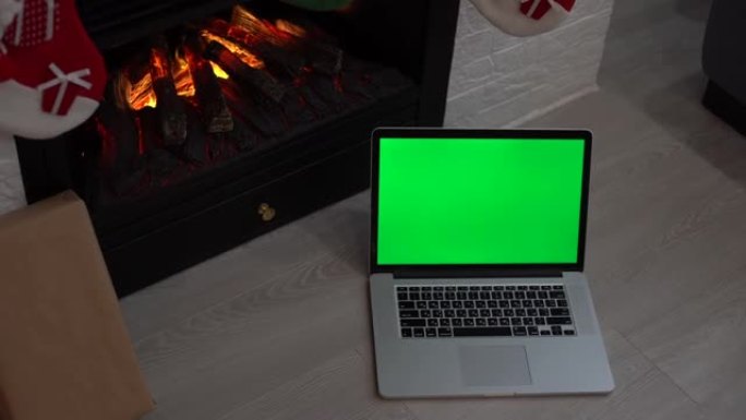 带有圣诞节背景的家庭工作笔记本。笔记本电脑的绿色屏幕。假日营业时间。壁炉附近的家庭工作场所