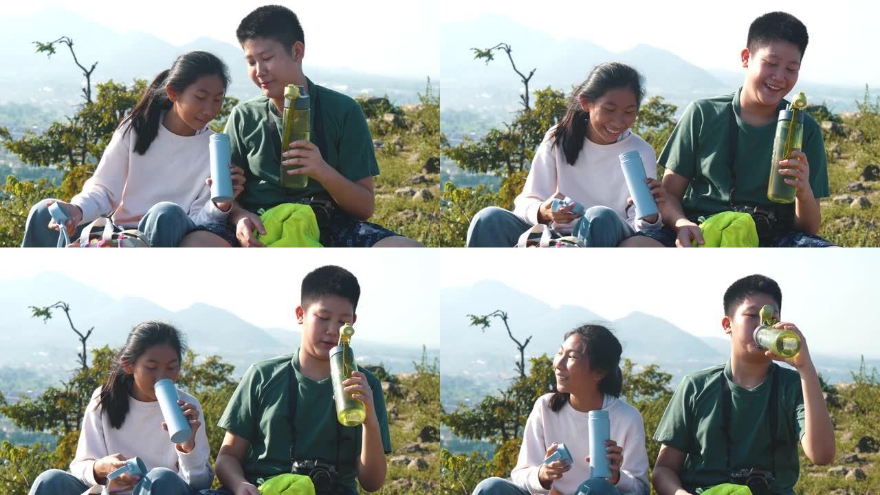 快乐的亚洲男孩和女孩在阳光明媚的户外冒险旅行中从自己的水食堂喝水。