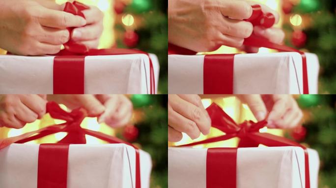 带有圣诞灯背景的礼品盒上的手系丝带。