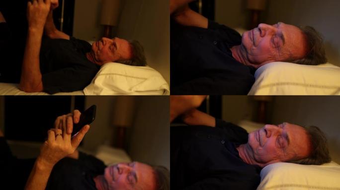 年长的男人拿起手机，躺在床上看着智能手机屏幕