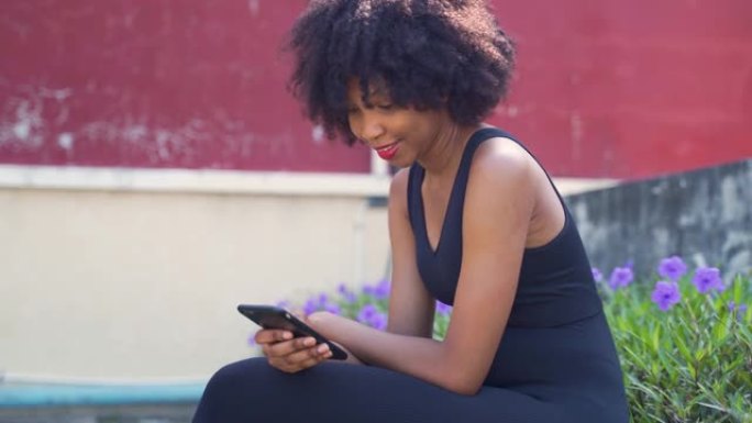 年轻的非洲裔美国妇女使用手机，坐在公园的长凳上。女性黑人慢跑者在户外休息和微笑
