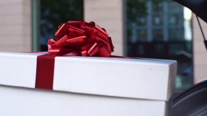 送货员的特写镜头从汽车后备箱中取出带有漂亮红色蝴蝶结的大型节日白色盒子。