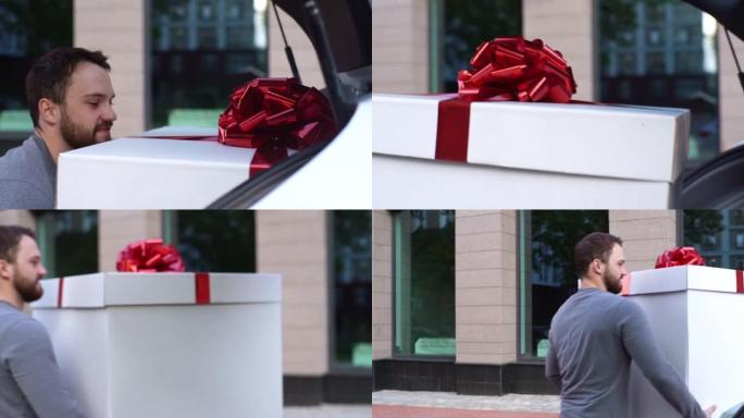 送货员的特写镜头从汽车后备箱中取出带有漂亮红色蝴蝶结的大型节日白色盒子。