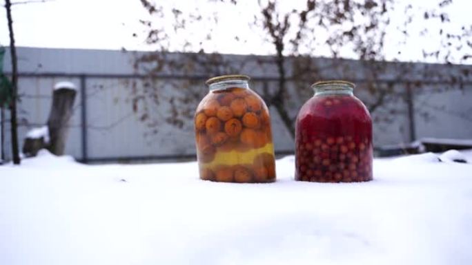 在街上的雪中关闭带有水果和浆果的罐装果汁。冬季在花园里密封的蜜饯罐